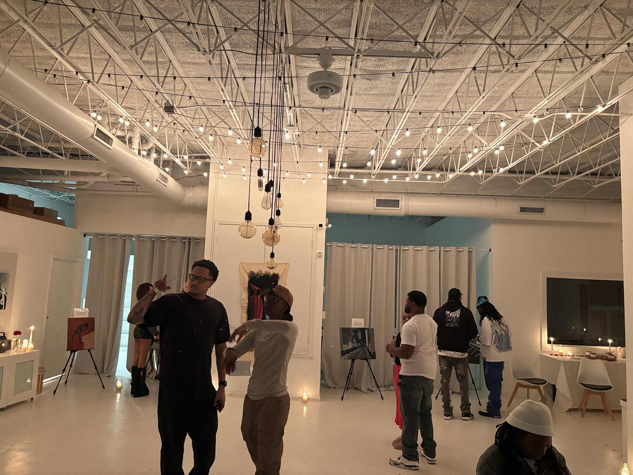 Wide view of the exhibition space under strings of bulb lights